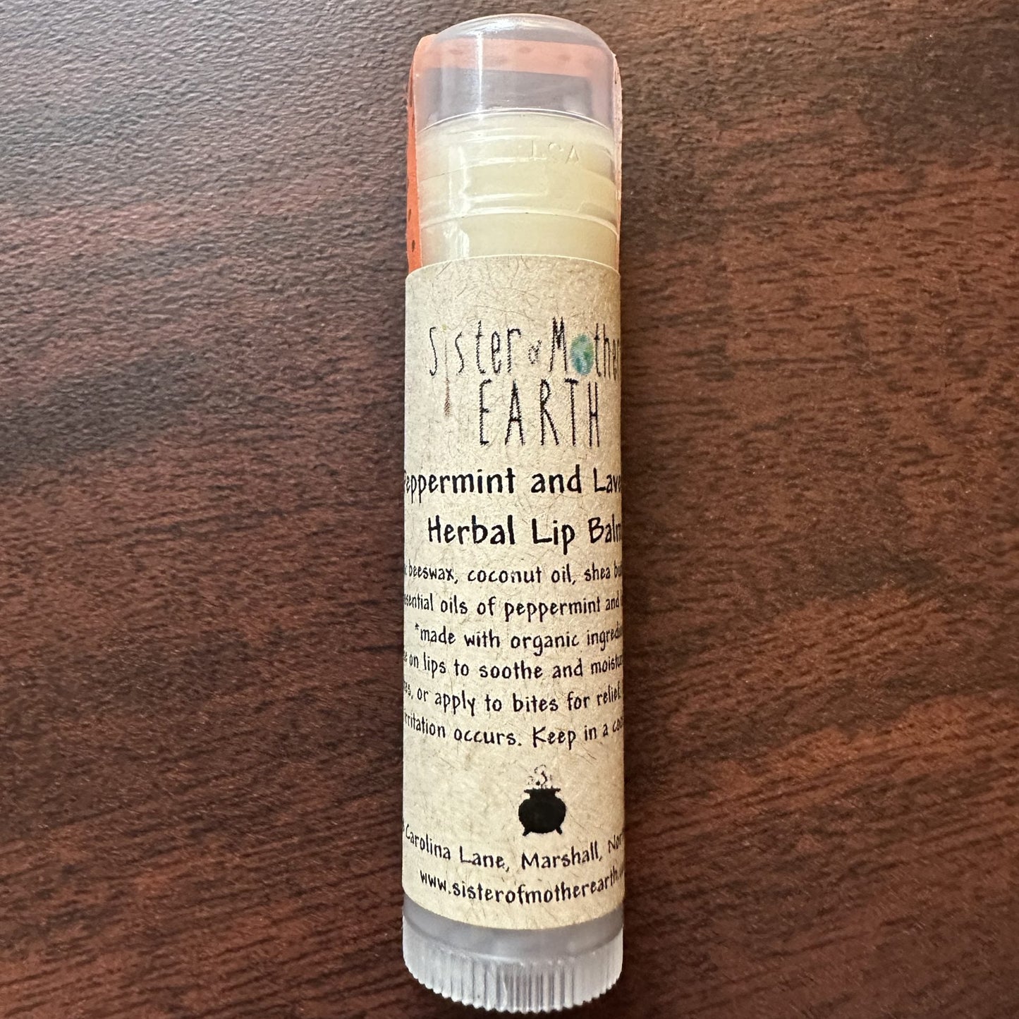 A stick of Sister of Mother Earth Peppermint and Lavender Herbal Lip Balm on a wooden surface.