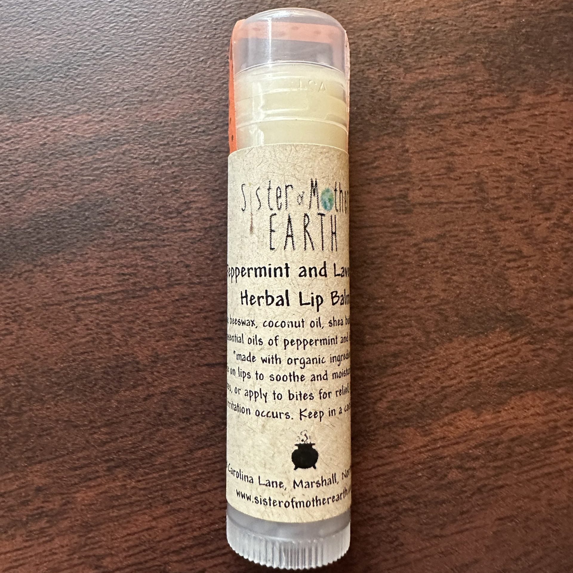 A stick of Sister of Mother Earth Peppermint and Lavender Herbal Lip Balm on a wooden surface.