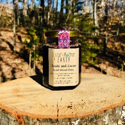 A hexagon jar of Sister of Mother Earth Reishi and Cacao Infused Honey placed on a wooden surface with a forest background.