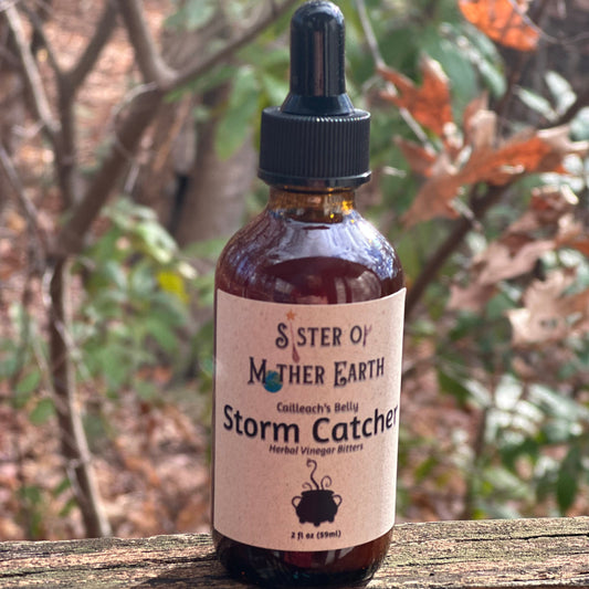 An amber glass dropper bottle of Storm Catcher vinegar bitters from Sister of Mother Earth stands in front of a woodland background.